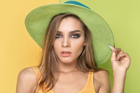 Summer vibes. Beautiful caucasian young woman posing in colorful hat, on yellow background.の写真素材