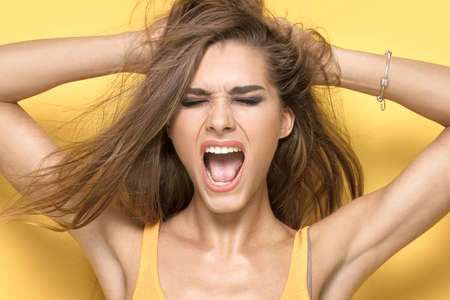 Attractive female model posing on yellow background, screaming loud.の写真素材