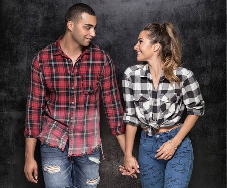 Young modern stylish couple in fashionable clothes over dark background. Beautiful caucasian girl posing with african american handsome man, couple smiling.の写真素材