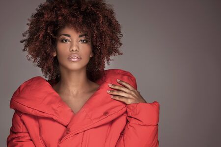 Fashion portrait of young beautiful african american woman with afro hairstyle. Girl with glamour makeup looking at camera, posing in red jacket.の写真素材