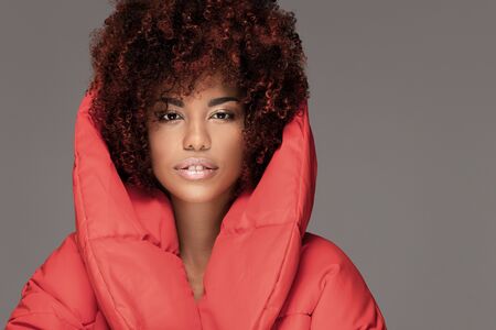 Fashion portrait of young beautiful african american woman with afro hairstyle. Girl with glamour makeup looking at camera, posing in red jacket.の写真素材
