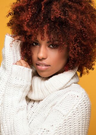 Young beautiful african american girl with an afro hairstyle. Attractive girl wearing cozy sweater....