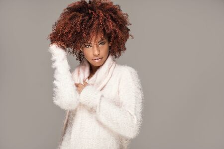 Happy beautiful african american girl with afro hairstyle posing in cozy sweater.の写真素材