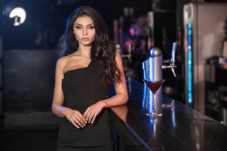 Elegant young woman standing at the bar, celebrating with drink, looking at camera.の写真素材