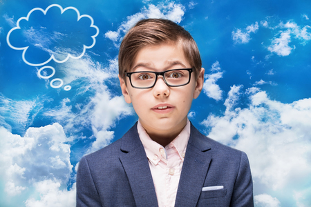 Kid in eyeglasses posing on blue sky background. Child Boy thinking, elegant little businessman in fashionable clothes.の写真素材
