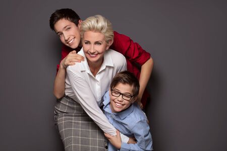 Happy family, elegant blonde caucasian mother having fun with two sons, smiling, playing. Studio...