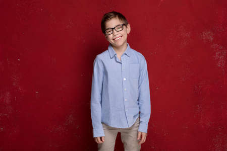 Kid in eyeglasses posing on red background. Child Boy smiling, elegant little businessman in fashionable clothes.の写真素材