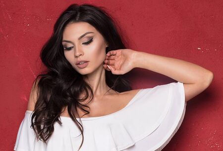 Attractive young woman with long hair and glamour makeup posing in white fashionable swimsuit on red background.の写真素材