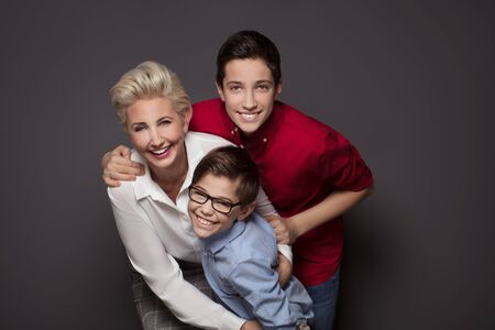 Happy family, elegant blonde caucasian mother having fun with two sons, smiling, playing. Studio shot.の写真素材