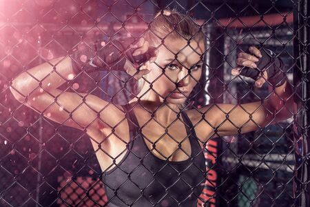 Female boxer standing inside a boxing cage. Attractive blonde woman with perfect fit bodyの写真素材