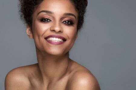 Beauty portrait of smiling dark skin young woman with curly afro hair and glamour makeup. Studio  shot on gray background, copy space.の写真素材