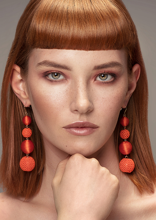Beauty portrait of redhead young lady with fringe, freckles on face. Girl wearing fashionable earrings, looking at camera.の写真素材