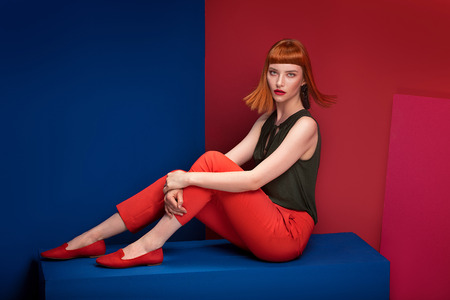 Fashionable redhead lady with fringe and glamour makeup posing over colorful background, looking at camera.の写真素材