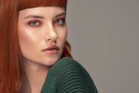 Beautiful natural redhead woman posing in fashionable sweater, looking at camera.の写真素材