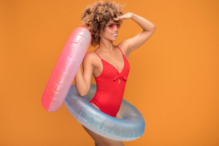 Photo of an excited african girl dressed in red swimsuit holding inflatable ring isolated over yellow background.の写真素材