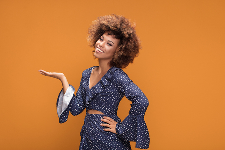 Happy beautiful african american woman posing in fashionable dotted dress, smiling, standing on yellow background.の写真素材