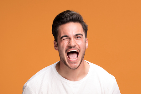 Young handsome man blinking eyes with happy gesture, yellow studio background.の写真素材