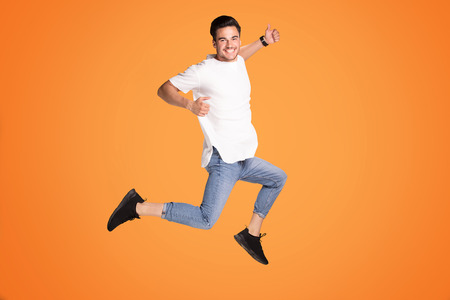 Full length photo of a smiling young man showing okay symbol and jumping isolated over yellow studio...