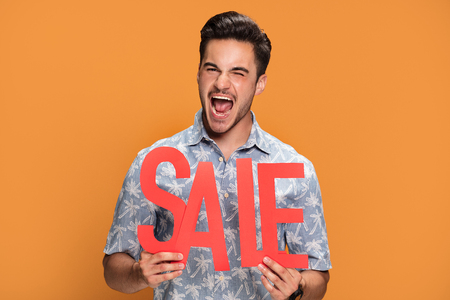 Smiling handsome man holding red sale letters on yellow studio background.の写真素材