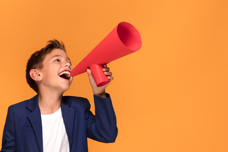 Little elegant boy with red megaphone on orange studio background.の写真素材