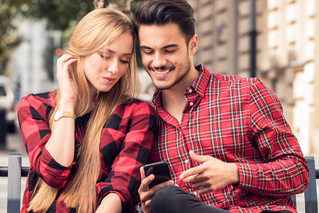 Smiling couple in love dating outdoors.Young happy couple sitting, looking at mobile phone.の写真素材