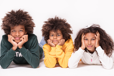 Happy smiling three afro children in colorful clothes laying on the floor, looking at camera.の写真素材