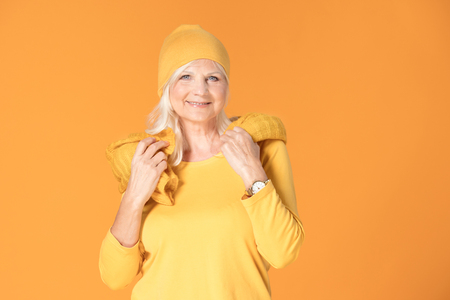 Smiling mature woman in yellow cap and scarf. Studio shot.の写真素材