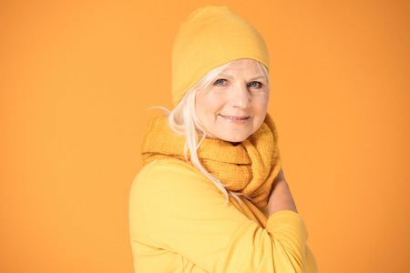 Smiling mature woman in yellow cap and scarf. Studio shot.の写真素材
