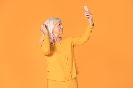 Studio shot of a beautiful senior woman posing with mobile phone on yellow background.