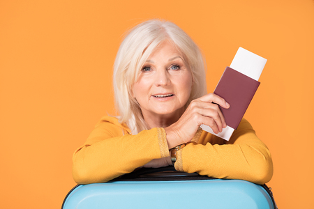 Senior woman with suitcase,passport and tickets on color background. Smiling beautiful lady.の写真素材