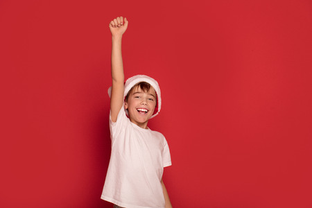 Smiling young happy boy posing in Santa Claus hat on red studio background. Christmas concept.の写真素材