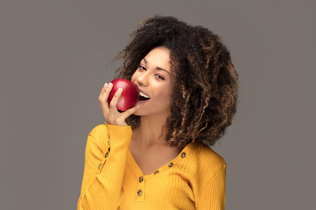 Healthy beautiful african american model with apple and open mouth looking at camera. Studio background.の写真素材