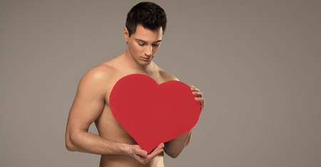 Handsome shirtless man posing with red heart, valentine's day.の写真素材