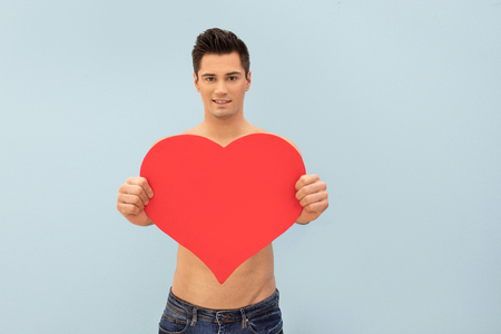 Handsome shirtless man posing with red heart, valentine's day.の写真素材