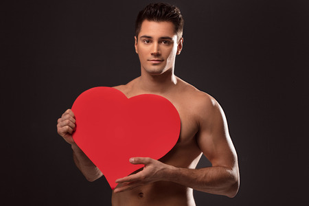 Handsome shirtless man posing with red heart, valentine's day.の写真素材