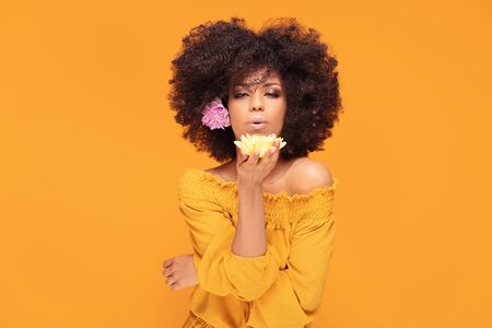 Beauty portrait of african american woman with glamour makeup, afro hair and fresh flowers in hand...