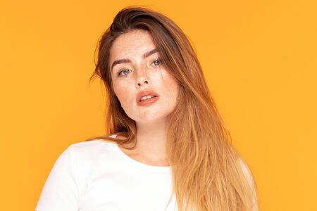 Beauty portrait od delicate caucasian lady. Beautiful ginger woman with long hair and with freckles posing on yellow studio background. Young attractive girl in white casual shirt.の写真素材
