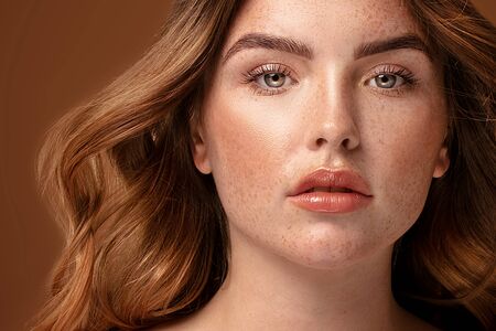 Beauty portrait od delicate caucasian lady. Beautiful ginger woman with long hair and with freckles posing on brown studio background.の写真素材