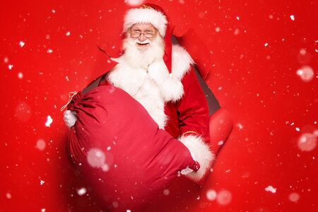 Santa Claus , the real one, comes out of the red studio background with a big gift. Christmas time.A lot of copy space.の写真素材