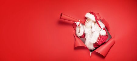 Santa Claus , the real one, comes out of the red studio background , screaming ho ho ho through big megaphone. Christmas time.の写真素材