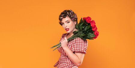 Attractive pinup girl holding red roses in hand. Beautiful woman with rollers on head.の写真素材