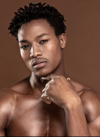 Fit young man looking at camera, posing isolated on brown background. Naked torso of African American man posing at studio. Muscular body, fitness, sports, healthy lifestyle and bodybuilder concept.の写真素材