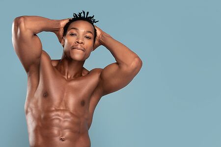Fit young man with beautiful torso, isolated on blue pastel background. Naked torso of African American man posing at studio. Muscular body, fitness, sports, healthy lifestyle and bodybuilder concept.の写真素材