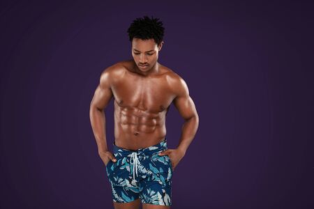 Fit young african man with beautiful torso, isolated on purple studio background. Muscular body, fitness, sports, healthy lifestyle and bodybuilder concept.の写真素材