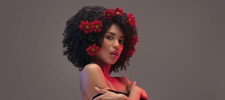 Young attractive afro woman with beautiful flowers in hair. Beauty studio portrait.の写真素材