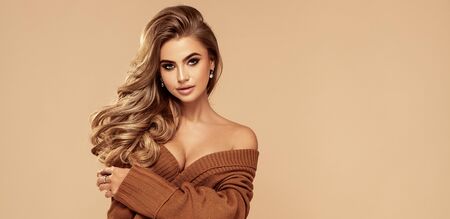 Young beautiful blonde woman wearing fashionable brown sweater over beige isolated studio background.の写真素材