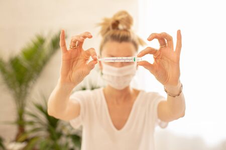 Woman measures the body temperature at home. Coronovirus Quarantine. Girl with a thermometer in her...