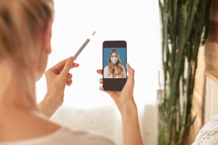 Sick patient have online video consultation with doctor on mobile phone, showing thermometer to the...