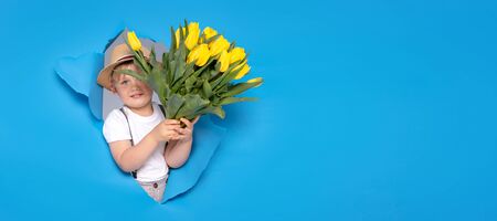 Young little caucasian kid holding yellow bouquet of flowers over blue background. Happy boy with smile. Mother's day.の写真素材
