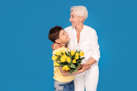 Boy holding a bouquet of yellow tulip flowers. Son gives his mother a gift for her birthday, March 8, mothers day. Happy family time.の写真素材